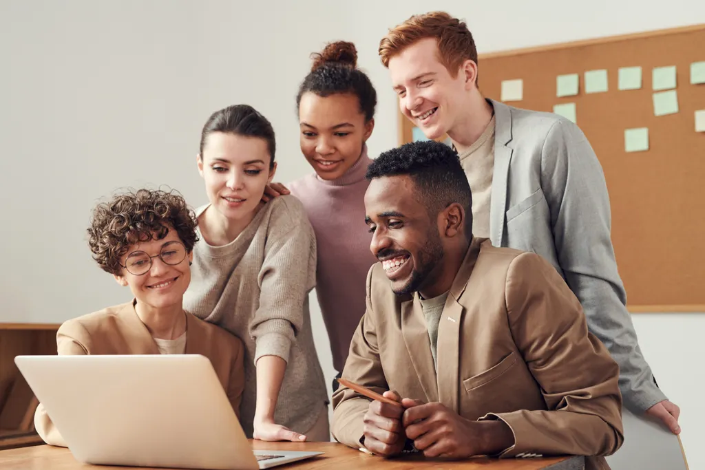 Five colleagues gathered around a laptop, smiling as they review work together