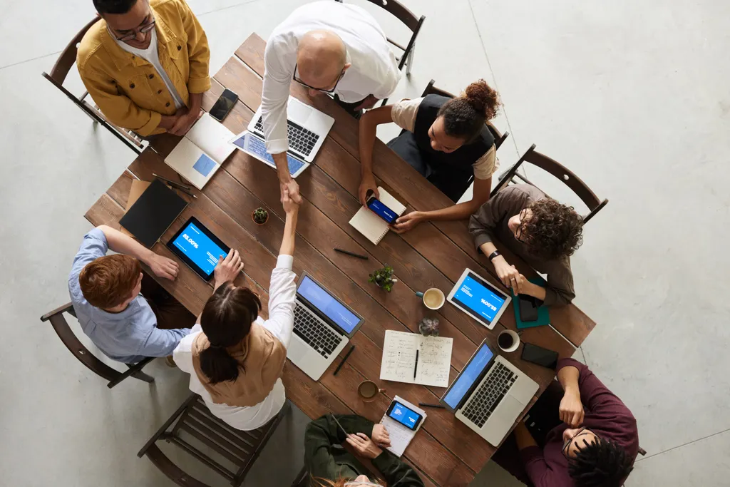Overhead view of colleagues shaking hands across a table of laptops and notebooks