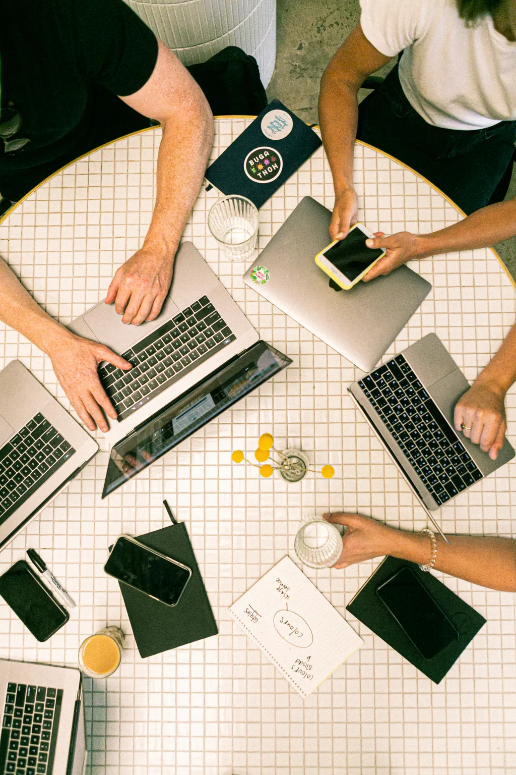Overhead view of people working on laptops around a white tiled table with a hand-drawn sketch